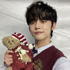 a young man holding a teddy bear wearing a sweater