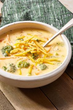 a bowl of broccoli cheese soup on a wooden table with a green napkin