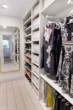 a walk in closet with white shelving and lots of clothes on shelves next to a mirror