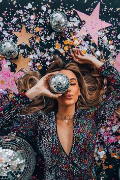 a woman holding a disco ball in front of her face surrounded by confetti and stars