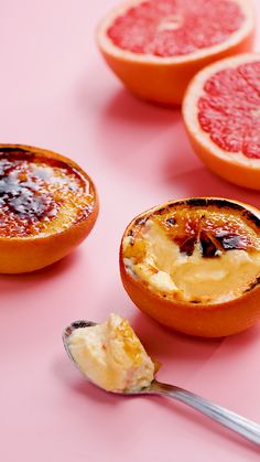 grapefruits are cut in half on a pink surface with a spoon next to them