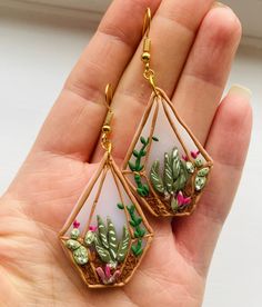 a pair of earrings with plants on them are being held in someone's hand