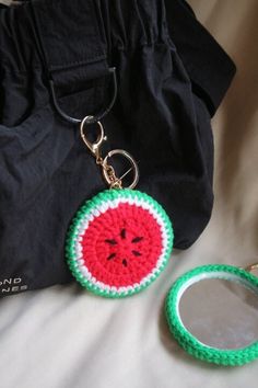 a watermelon keychain and mirror on a bed with a black bag