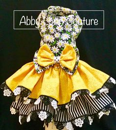 a yellow dress with black and white flowers on the bottom, has a large bow at the waist