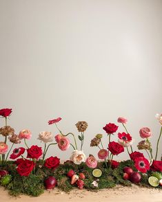 an arrangement of flowers on a table with moss and other things in the background,