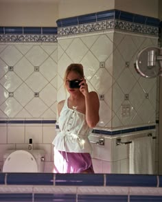 a woman taking a selfie in front of a bathroom mirror with her cell phone