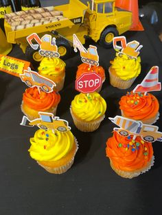 cupcakes with yellow frosting and construction themed toppers are on a table