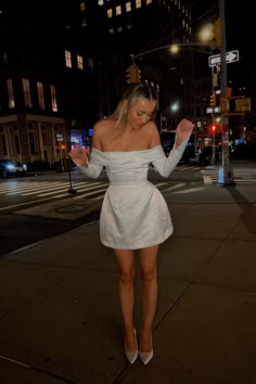 a woman in a short white dress is walking down the street with her arms outstretched