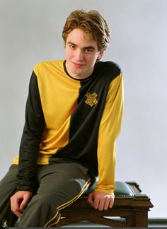 a young man sitting on top of a wooden table wearing a yellow and black shirt