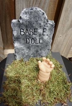 a tombstone with moss growing on it and a fake hand sticking out of the ground