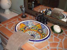 a bathroom sink with an artistic design on the bowl and mirror above it, next to a toilet