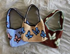 three crocheted purses sitting on top of a white bed next to each other