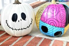 two painted pumpkins sitting on the ground next to each other with faces drawn on them