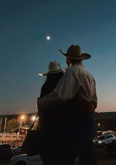 two men in cowboy hats standing next to each other on a parking lot at night