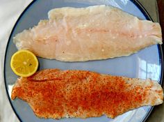 two fish fillets on a plate with lemon wedges and seasoning next to them