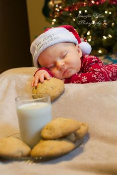 a baby laying on top of a bed next to cookies and a glass of milk