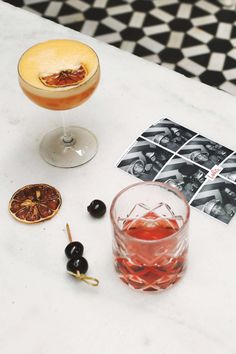 two cocktails on a marble table with black olives and an old - fashioned photo