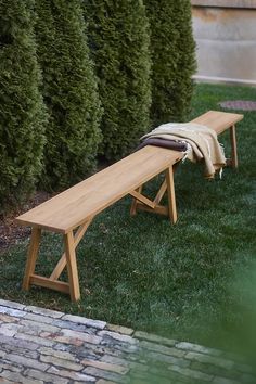 a wooden bench sitting in the grass next to some bushes and trees with a blanket on it