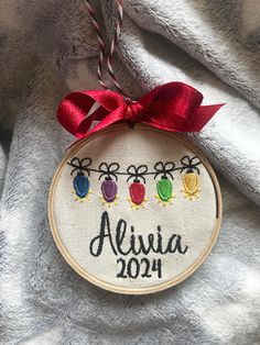 an embroidered christmas ornament hanging on a gray blanket with red ribbon and twinklings