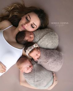 a woman is holding two babies in her arms and posing for the camera while laying down