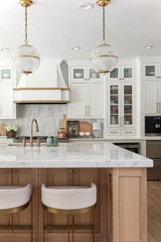 a large kitchen with white cabinets and marble counter tops, two stools in front of the island