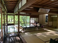 two people sitting on a bench in a room with wood flooring and large windows