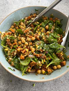 a bowl filled with spinach and chickpeas next to a pair of tongs