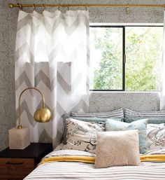 a bed sitting under a window next to a lamp and a wooden dresser in front of it