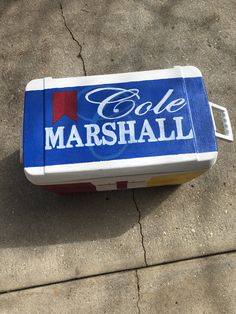 a cooler with the word cole marshall written on it is sitting on the sidewalk next to a curb