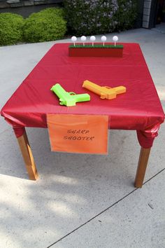 a red table topped with an orange and green plastic toy airplane next to a sign