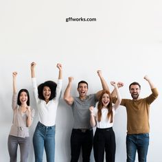 four people standing in front of a white wall with their arms up