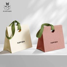 two paper bags with green ribbons on them sitting side by side in front of a white background