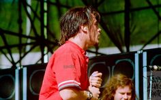 a man with long hair wearing a red shirt and holding a microphone in his hand