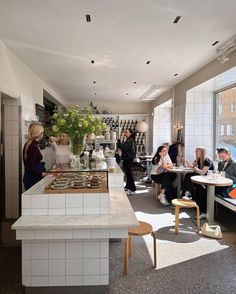 people sitting at tables in a restaurant with large windows and white tiles on the walls