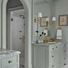 a bathroom with marble counter tops and gold accents on the sink, along with two white vases filled with flowers