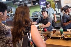 a group of people sitting at a table with food in front of them and one person standing behind the counter