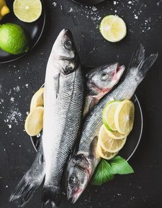 two fish and lemons on a plate next to some limes, salt and pepper