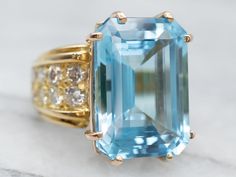 Here’s a super sparkly cocktail ring! This ring features rows of twinkling diamonds, with a bright blue emerald cut blue topaz center. Perfect for a birthstone or anniversary piece, this ring is icy and cool, and utterly lovely!Metal: 14K Yellow GoldGem: Blue Topaz 16.58 CaratsGem Measurements: 12.9 x 17.9 mm, Emerald CutAccents: 12 Diamonds totaling 1.24 Carats, F-H in Color, VS-SI in Clarity Ring Size: 6.25Marks: "14K" Stamped on the inside band Luxury Unique Yellow Gold Topaz Ring, Luxury Dazzling Gold Topaz Ring, Blue Emerald-cut Topaz Ring With Diamond Accents, Emerald Cut Topaz Ring With Diamond And Gemstone Accents, Gold Topaz Ring, Blue Emerald, Gold Topaz, Diamond Cocktail Ring, Topaz Jewelry