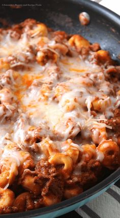 a skillet filled with pasta and meat covered in cheese on top of a table