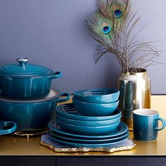 a table topped with lots of blue dishes next to a vase filled with peacock feathers