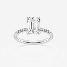 an emerald cut diamond engagement ring with diamonds on the band and side stones set in 18k white gold