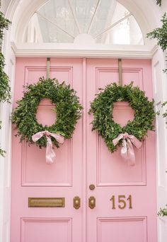 two wreaths on the front door of a pink house with ribbon tied around them