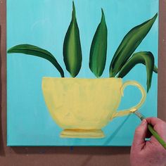 a person is painting a yellow cup with green plants in it on a blue background