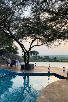 an outdoor dining area next to a swimming pool with a tree in the middle and chairs around it