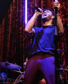 a man singing into a microphone while standing in front of a drum kit and drums