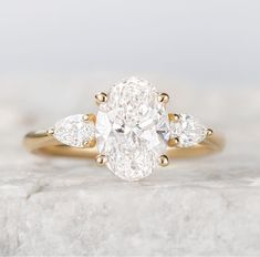 an oval diamond ring with three pear shaped diamonds on the band and side stones in yellow gold