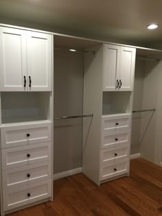 an empty walk in closet with white cabinets and drawers on the wall, next to a hardwood floor