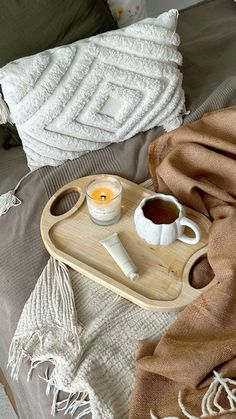 a tray with a candle, cup and saucer sitting on top of a bed