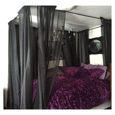 a bed with purple sheets and black drapes on the headboard, in a bedroom