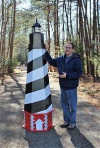 a man standing next to a black and white striped light house in the middle of a forest